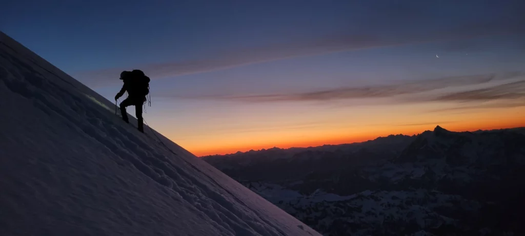 climber ascending boulder glacier at sunrise